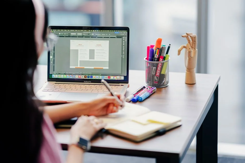 A photographer working at a creative setup with a laptop and Wacom tablet, focused on editing photos indoors.
